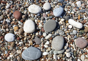 Multicolored large pebbles of various shapes on the sandy shore of the Mediterranean sea for backgrounds