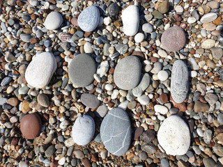 Multicolored large pebbles of various shapes on the sandy shore of the Mediterranean sea for backgrounds