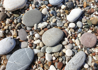 Multicolored large pebbles of various shapes on the sandy shore of the Mediterranean sea for backgrounds