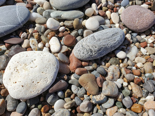 Multicolored large pebbles of various shapes on the sandy shore of the Mediterranean sea for backgrounds