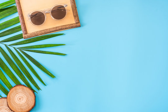 summer blue banner with wood picture grame ,sunglasses,seashell and palm leaf on blue background top view.