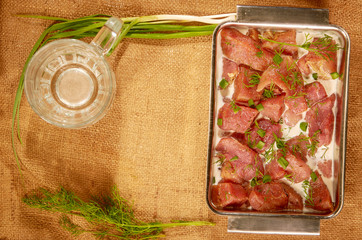 Marinated in milk and greens meat in a steel dish on a cloth with fresh herbs and a mug for beer