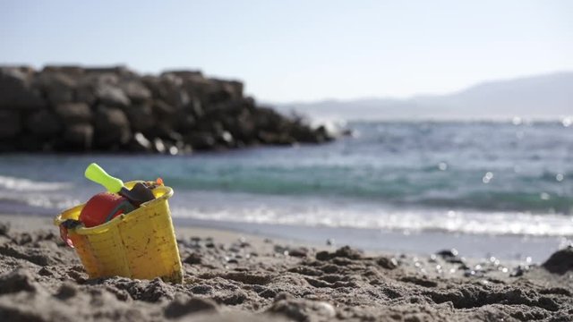 A bucket and spade on a sandy beach in Gibraltar with the sea in the background, waves wash up on shore