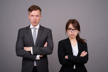 Young businessman and young Asian businesswoman against gray bac