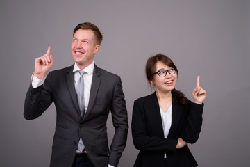 Young businessman and young Asian businesswoman against gray bac