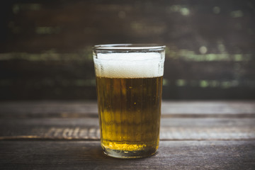 Glass of beer on the dark rustic wooden background. Selective focus. Shallow depth of field.