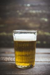 Glass of beer on the dark rustic wooden background. Selective focus. Shallow depth of field.