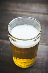 Glass of beer on the dark rustic wooden background. Selective focus. Shallow depth of field.