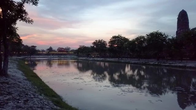 Panning shot across calm, peaceful lake reflecting mirror image of Ayutthaya temple sunset, Thailand.