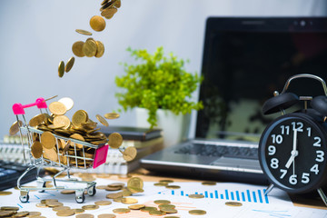 Falling gold coins in shopping cart or supermarket trolley on working table with office supplies or office work essential tools items