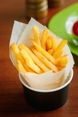 French fries rolled in parchment inside black cup on table.