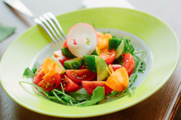 Salad with cherry potatoes, cucumber, raddish and lettuce in a green plate.