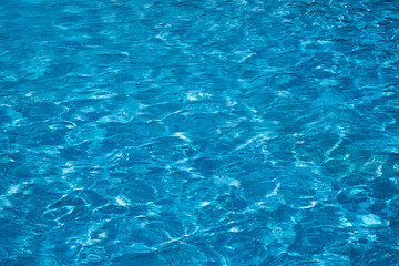 Blue and bright ripple water surface in swimming pool with sun reflection.