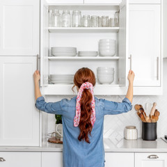 A woman looking in a farmhouse kitchen cabinet full of white dishes