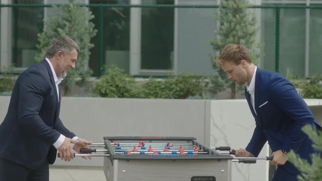 Two business partners have a leisure time together and play table football outside of office. 