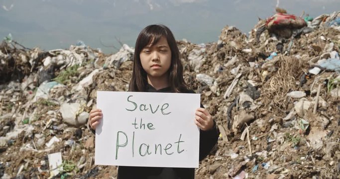 Asian kid on dump site holding ecological slogans, little activist fighting against pollution - environmental issue concept 4k close up