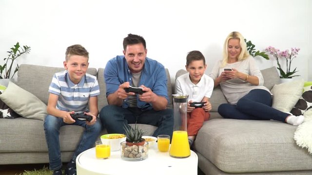 A happy family on a couch. A father playing video games with his two sons, mother watching them and laughing. 