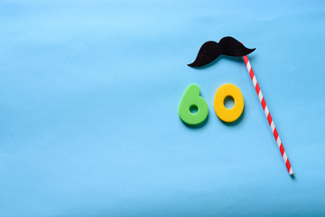 60 celebrating yellow green number with  mustache cute paper mask on straw stick.Sixty Modern alphabet digits on blue background. 60 th birthday party anniversary card.Flat lay, top view.Copy space