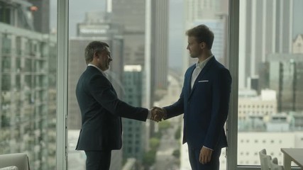 Two business partners do handshake in front of view on downtown and skyscrapers. A good business deal. - Powered by Adobe
