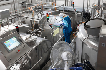 worker in a blue robe and a cap inspect the production department of dairy factory