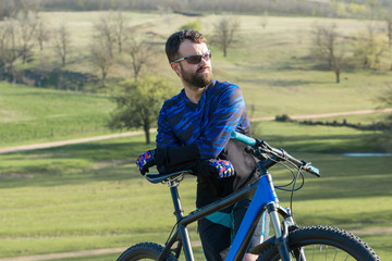 Fototapeta premium Cyclist in shorts and jersey on a modern carbon hardtail bike with an air suspension fork rides off-road on green hills near the forest 