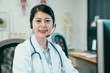 female doctor wearing headset while using computer at desk in clinic office. beautiful woman...