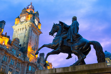 Fototapeta na wymiar Statue of Wellington on horseback silhouetted against a blue sky, with the clock tower of Balmoral Hotel in the background