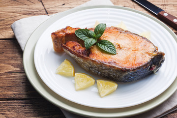 Steak baked fish salmon on a plate with lemon. Wooden table.
