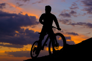 Cyclist in shorts and jersey on a modern carbon hardtail bike with an air suspension fork rides off-road on the orange-red hills at sunset evening in summer