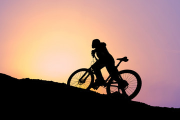 Obraz premium Cyclist in shorts and jersey on a modern carbon hardtail bike with an air suspension fork rides off-road on the orange-red hills at sunset evening in summer