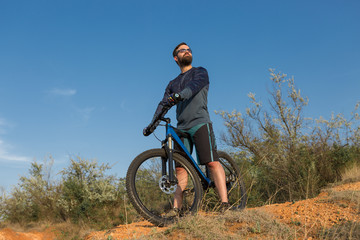 Naklejka premium Cyclist in shorts and jersey on a modern carbon hardtail bike with an air suspension fork rides off-road on the orange-red hills at sunset evening in summer