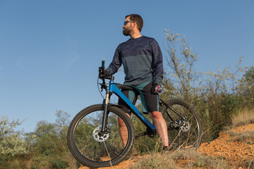 Obraz premium Cyclist in shorts and jersey on a modern carbon hardtail bike with an air suspension fork rides off-road on the orange-red hills at sunset evening in summer