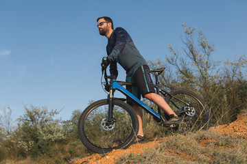 Obraz premium Cyclist in shorts and jersey on a modern carbon hardtail bike with an air suspension fork rides off-road on the orange-red hills at sunset evening in summer