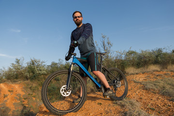 Fototapeta premium Cyclist in shorts and jersey on a modern carbon hardtail bike with an air suspension fork rides off-road on the orange-red hills at sunset evening in summer