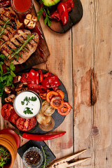 Grilled meat. Steak pork grill on wooden cutting board with a variety of grilled vegetables on  rustic background  Top view. Flat lay. Copy space.