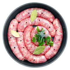 Delicious rustic raw  meat sausages in frying pan, with bay leaves and fresh herbs in the kitchen.
