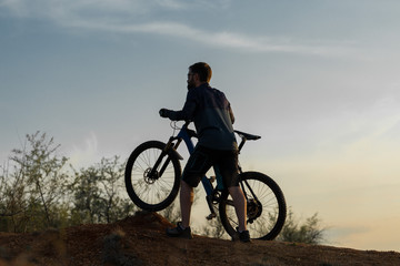 Fototapeta na wymiar Cyclist in shorts and jersey on a modern carbon hardtail bike with an air suspension fork rides off-road on the orange-red hills at sunset evening in summer