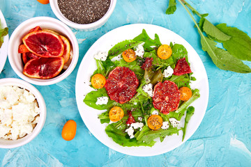 Fresh Citrus Salad with arugula feta, chia, kumquat and blood orange on blue background . Vegan, vegetarian, clean eating, dieting, food concept. Top view, flat lay, copy space