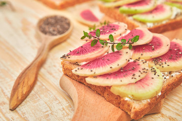 Healthy breakfast toasts from sliced watermelon radish or chinese daikon, chia and cottage cheese on board wooden background. Copy space.