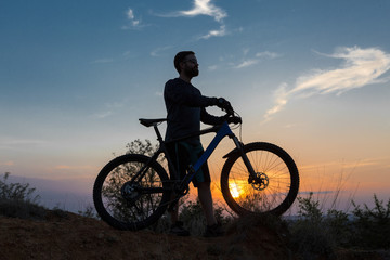 Obraz na płótnie Canvas Cyclist in shorts and jersey on a modern carbon hardtail bike with an air suspension fork rides off-road on the orange-red hills at sunset evening in summer
