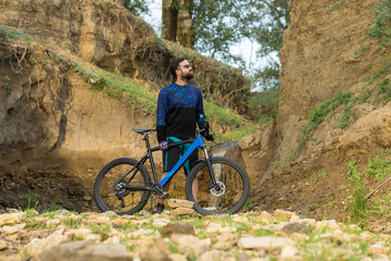 Obraz premium Cyclist in shorts and jersey on a modern carbon hardtail bike with an air suspension fork stands on the rocky shore of a mountain river