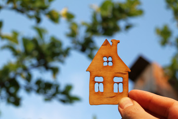 Layout of a wooden house in hand on the background of trees in the garden. new house with windows