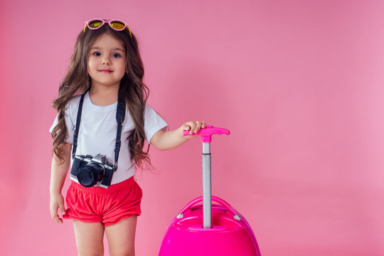 Portrait of little traveler girl on travel case with hat photo camera and passport ticet on pinc studio