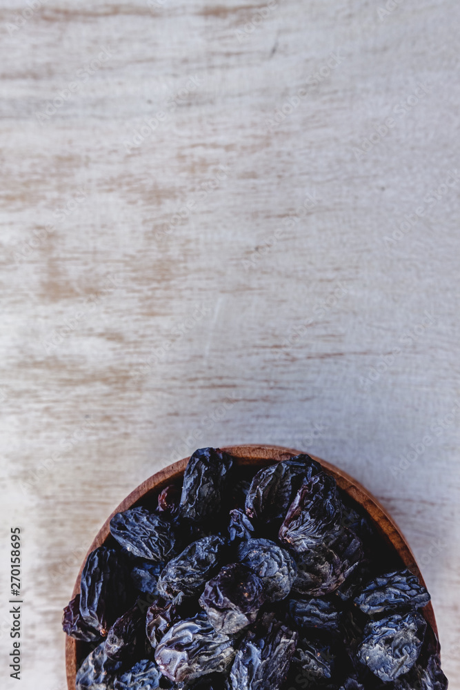 Wall mural dark blue raisins in a wooden bowl on a bright white background. close-up. insulated.