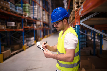 Warehouse worker checking inventory in large distribution center. Controlling goods storage and distribution.