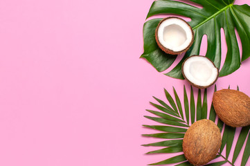 Tropical leaves and fresh coconut on pink background. Flat lay, top view, copy space. Summer background, nature. Healthy cooking. Creative healthy food concept, half of coconut