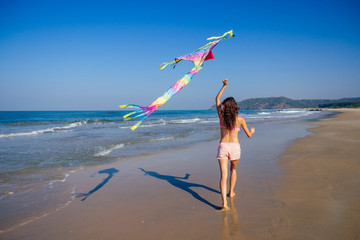 happy brunette girl in a bathing suit and short pink playing with flying kite on tropical beach...