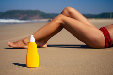 beautiful tanned female fitness big boobs model spf applying on the long legs in a fashion stylish swimsuit on sea ocean beach blue sky and palm trees background.summer vacation epilation depilation