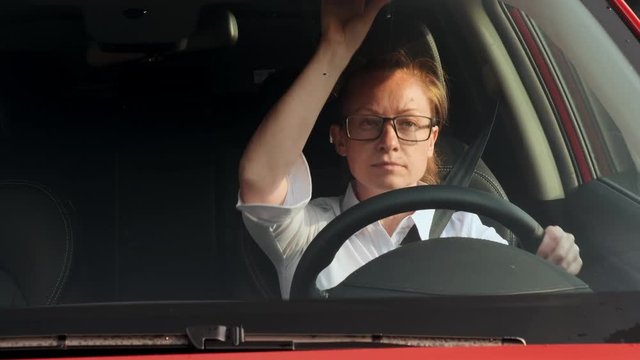 Satisfied business woman makes makeup looking in mirror in sun visor while driving. young businessman traveling to a meeting in the car.