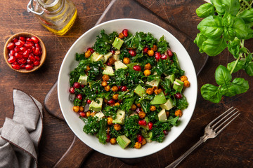 avocado, kale, roasted chickpeas, almond and pomegranate salad in white bowl, healthy vegan food,  top view, wooden background